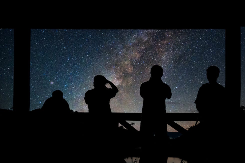 silhouette of a photographers group who shoots the landscape of milky way over reservoir with mountain and deep forest at night sky