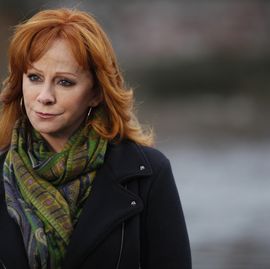 reba mcentire wears a green colorful scarf and black jacket as she looks to the left with a solemn expressions