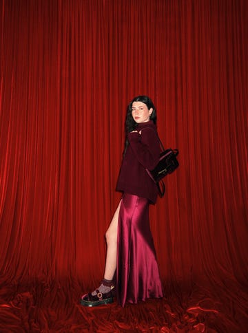 a person wearing a burgundy outfit stands against a red backdrop