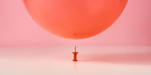 red balloon fall on a pin needle on pink background danger or protection concept