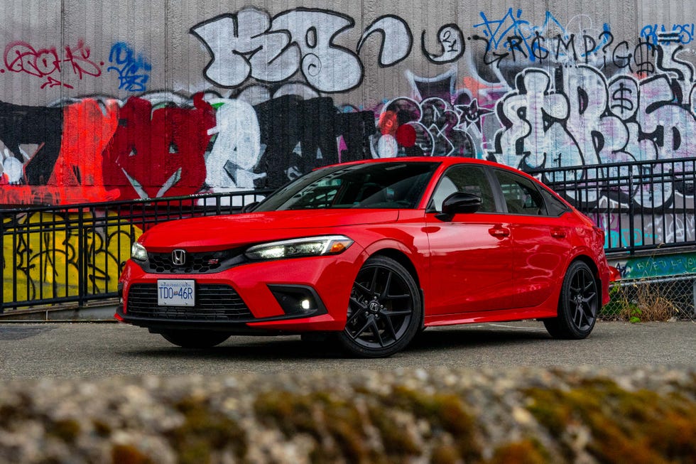 A red car is parked in front of a wall with graffiti