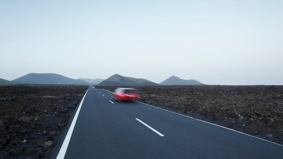 Red car in blurred motion travelling on straight road crossing lava plains towards distant volcanoes. red car in blurred motion travelling on straight road crossing lava plains towards distant volcanoes