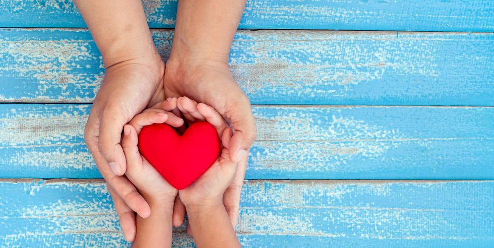 red heart in child kid and mother hands on old blue wooden table