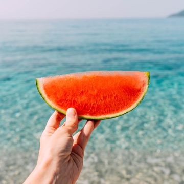 red piece of watermelon in hand against the background of the blue sea.