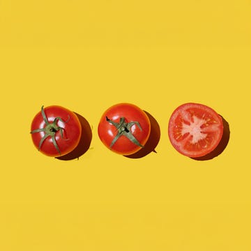 three red tomatoes on a yellow background two whole and one sliced