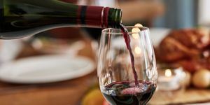 red wine, hand and pour at christmas feast or celebration holiday, event or festive season glass, alcohol or bottle closeup for drink at party table for lunch food, social gathering or vacation meal
