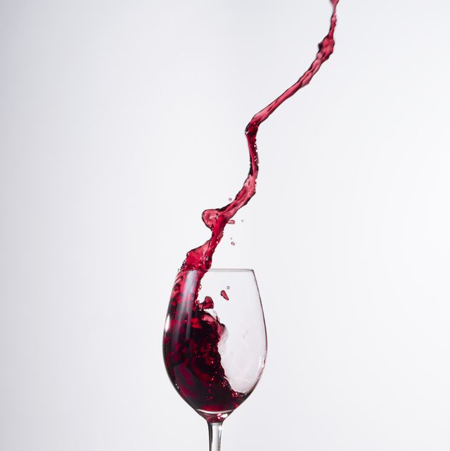 Red wine splashing in glass in front of white background.