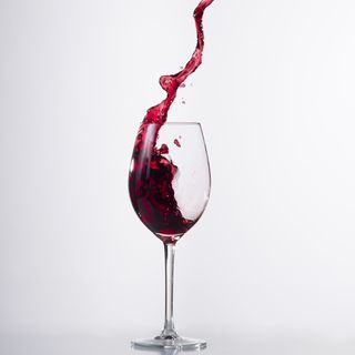 Red wine splashing in glass in front of white background.