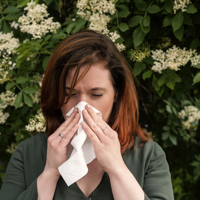 a redhead woman suffers from hay fever and sneezes into a handkerchief
