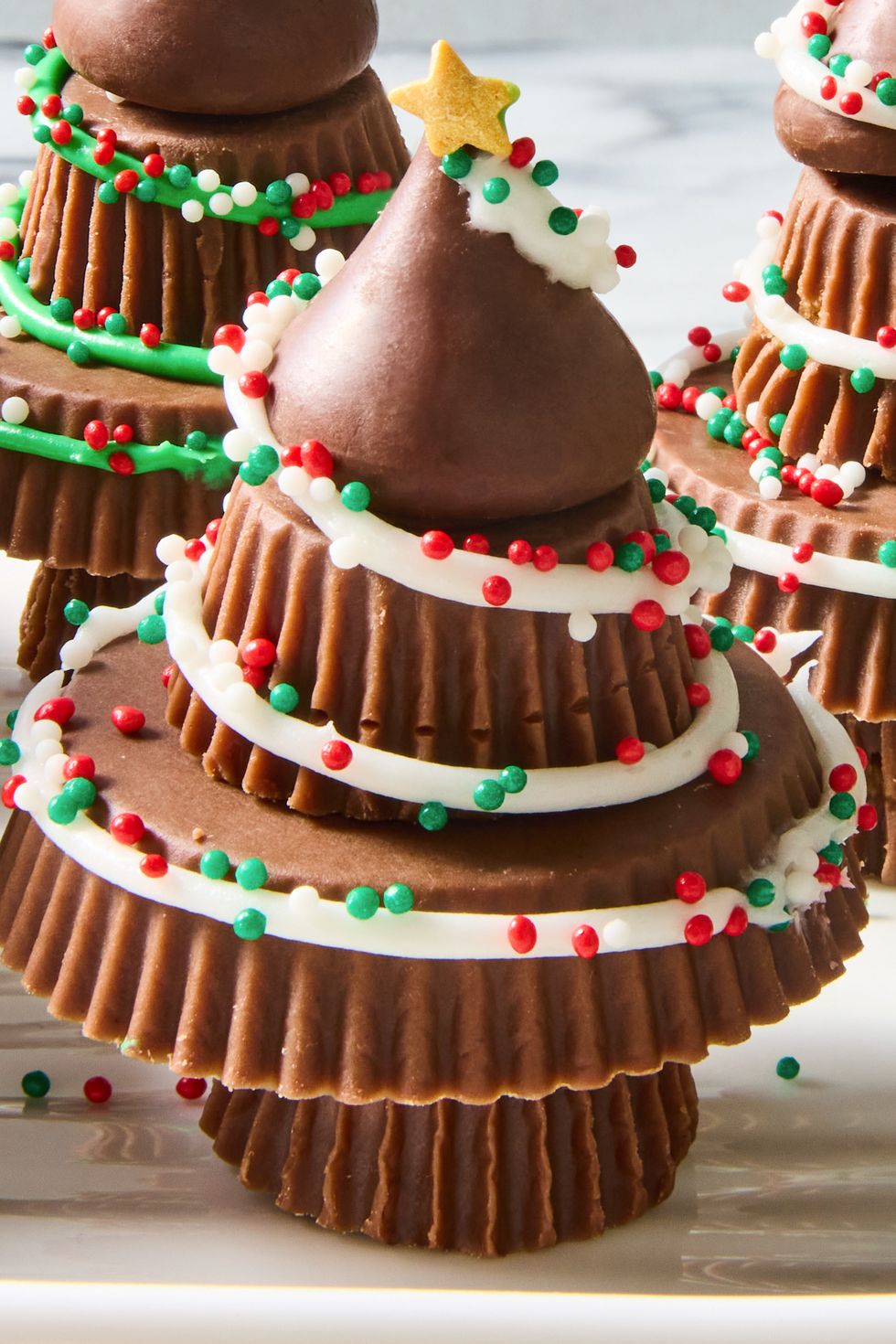 stacks of mini reeses peanut butter cups decorated with white and green royal icing and red green and white nonpareil and star sprinkles to look like christmas trees