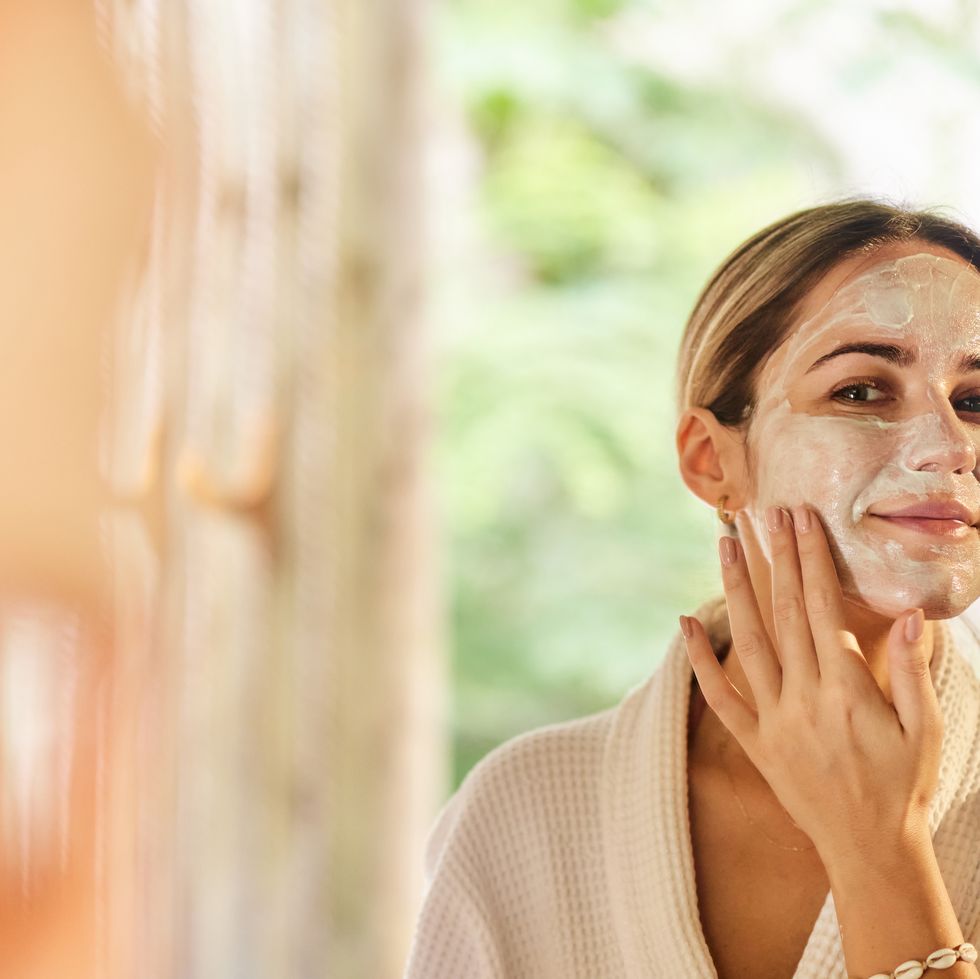 reflection in a mirror of smiling woman applying moisturizer.
