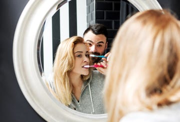 Reflection Of Couple Brushing Teeth In Mirror At Bathroom