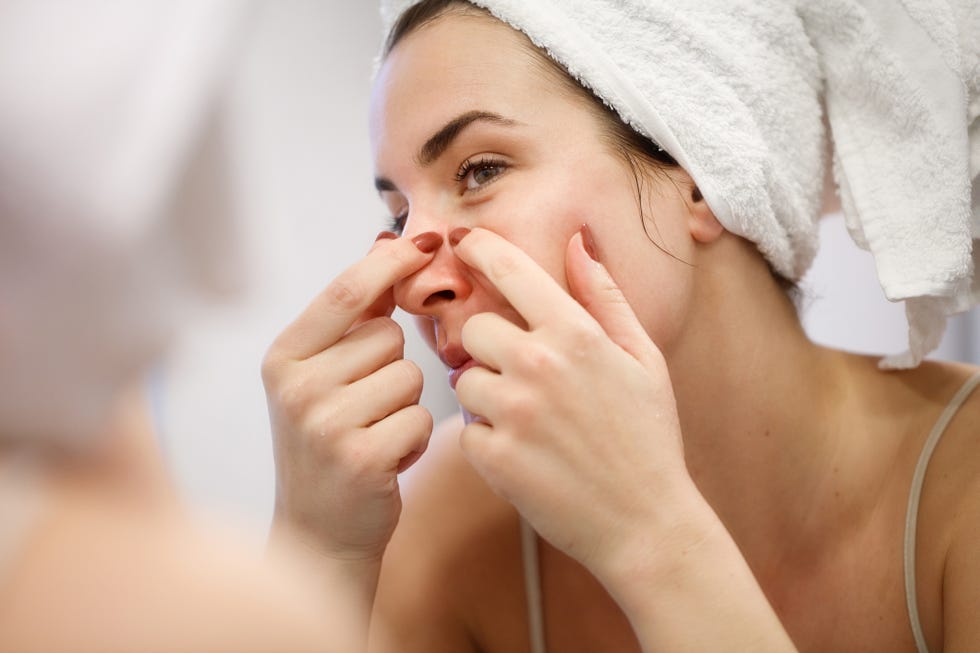 reflection of woman with towel on head squeezing blackhead on her nose side