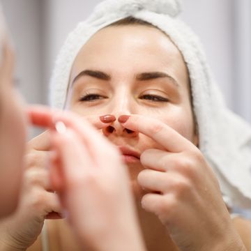 reflection of woman with towel on head squeezing blackhead on her nose