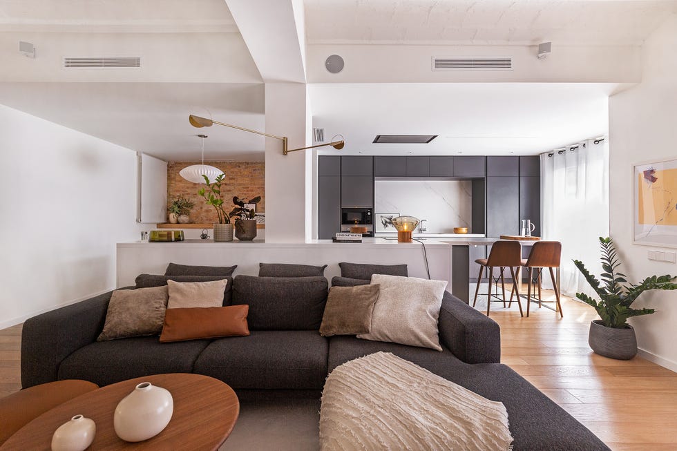salón abierto a la cocina y al comedor decorado en tonos neutros y estilo contemporáneo con una pared de ladrillo visto