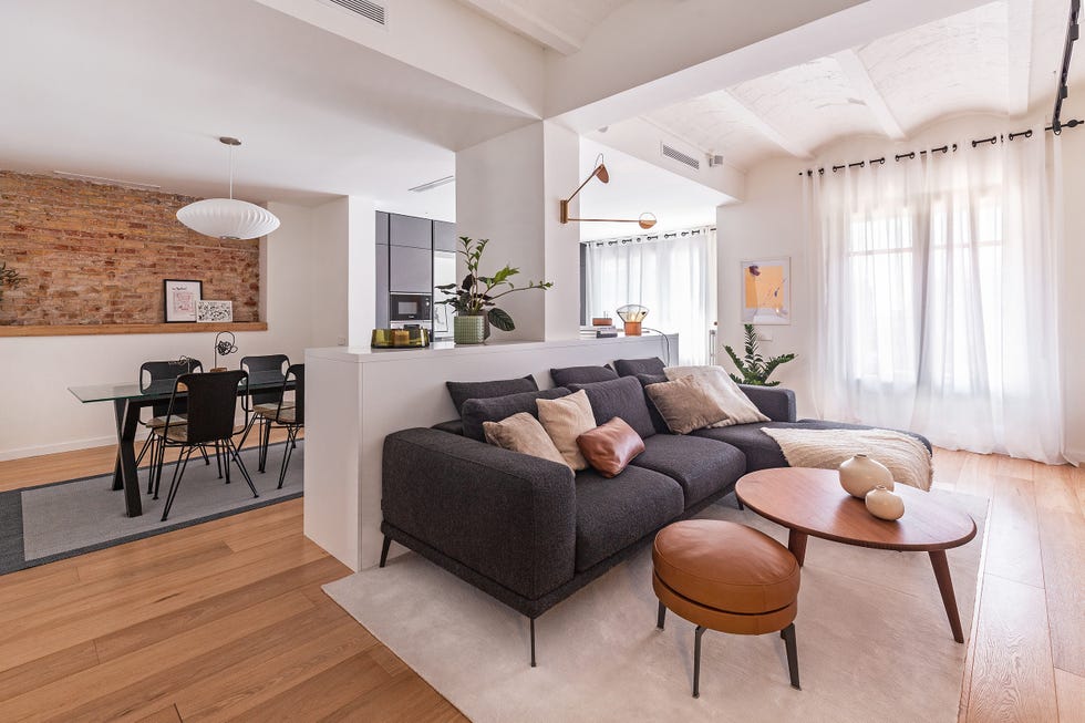 salón abierto a la cocina y al comedor decorado en tonos neutros y estilo contemporáneo con una pared de ladrillo visto