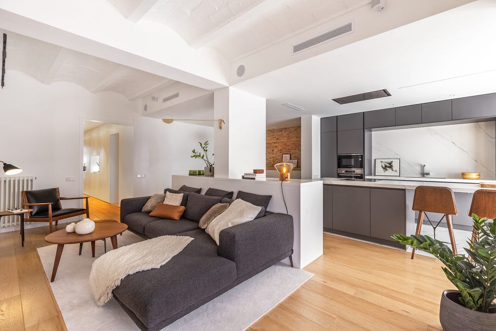 salón abierto a la cocina y al comedor decorado en tonos neutros y estilo contemporáneo con una pared de ladrillo visto