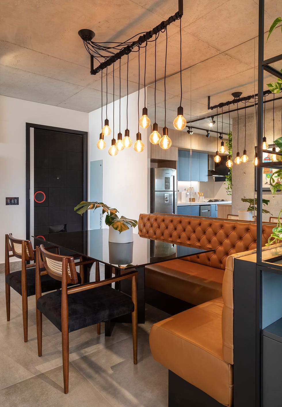 comedor abierto de estilo industrial con banco tapizado en piel marrón capitoné y mesa de cristal negro