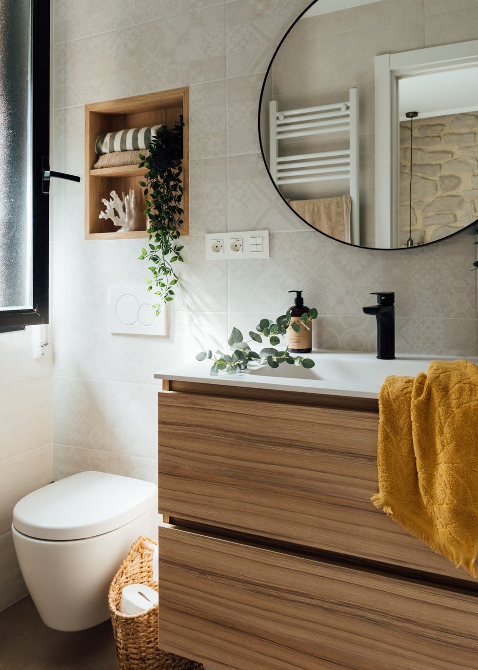 baño con mueble de madera suspendido, espejo redondo y hornacina de madera