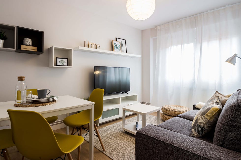 salón comedor de estilo nórdico con sofá gris, muebles blancos y sillas mostaza
