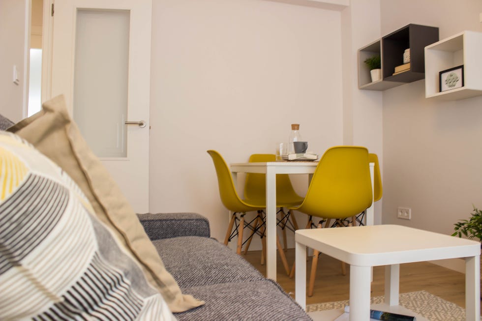 salón comedor de estilo nórdico con sofá gris, muebles blancos y sillas mostaza