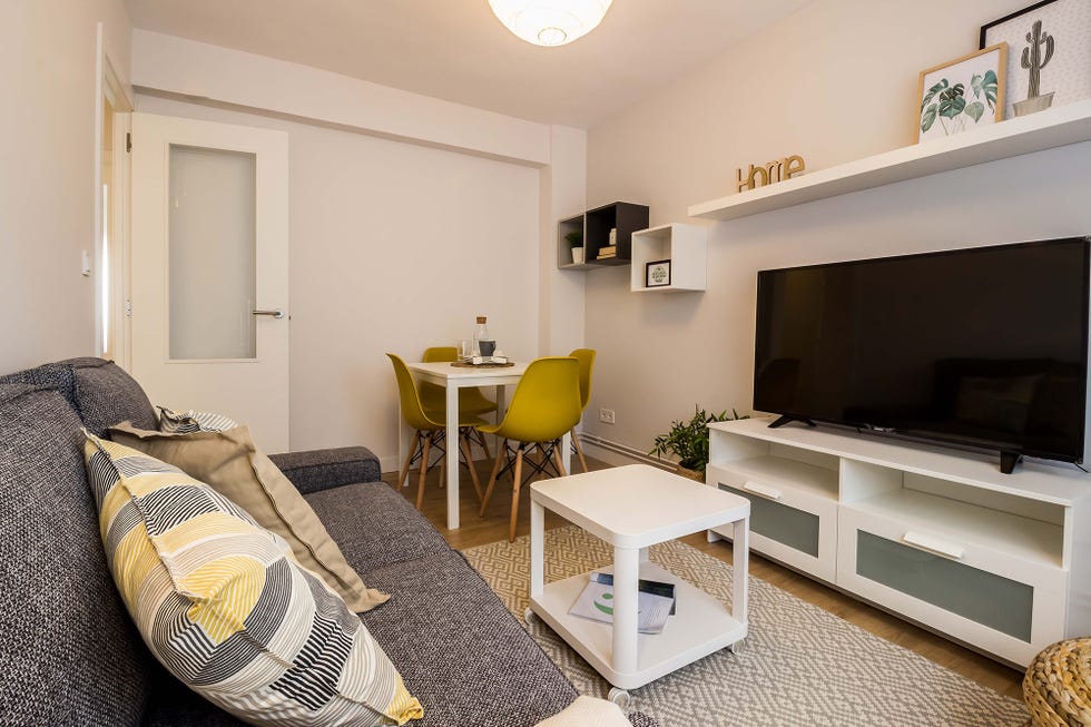 salón comedor de estilo nórdico con sofá gris, muebles blancos y sillas mostaza