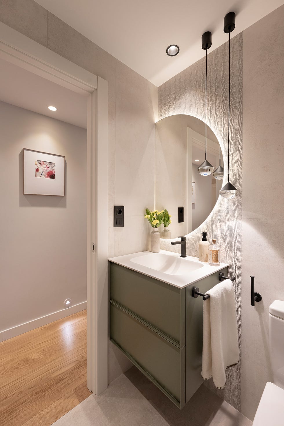 mueble de baño volado con cajones y espejo redondo junto a lámparas suspendidas