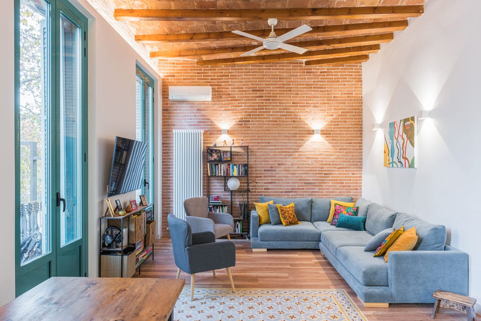 salón con pared de ladrillo visto y sofá esquinero gris y dos butacas