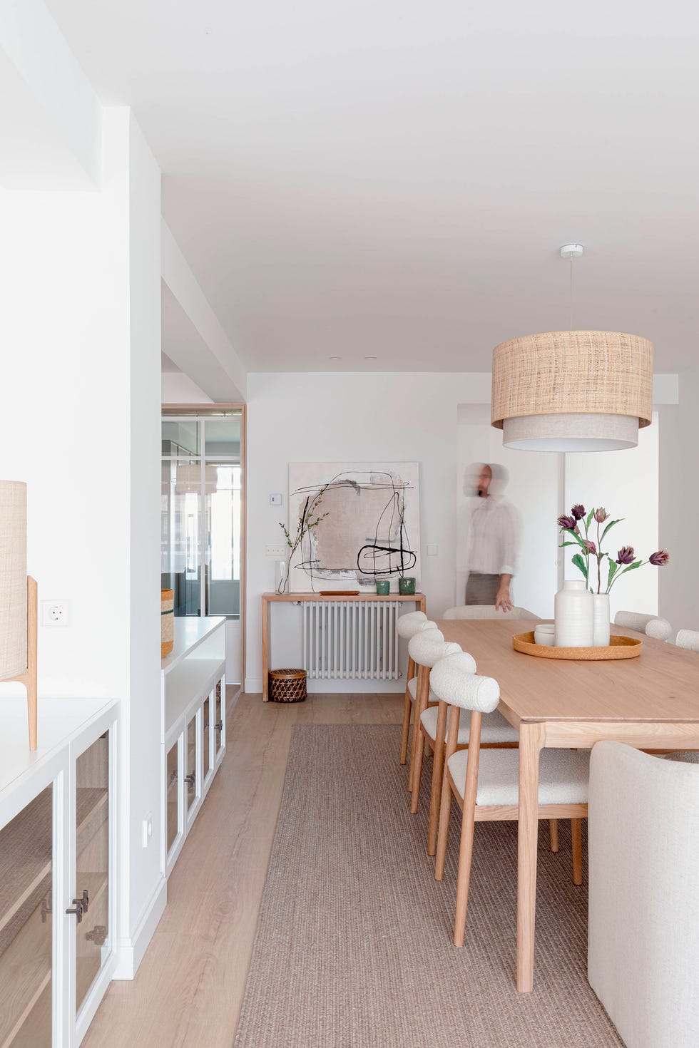 mesa de comedor de madera con sillas con tapizado bouclé y lámpara suspendida con pantalla de ratán