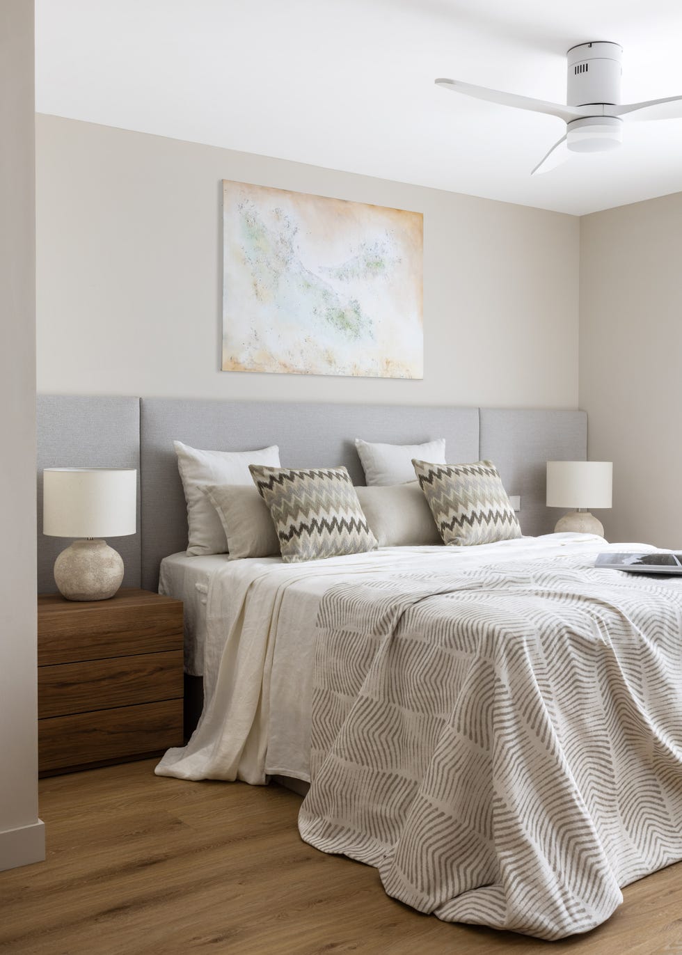 dormitorio con cabecero acolchado gris y mesitas de madera