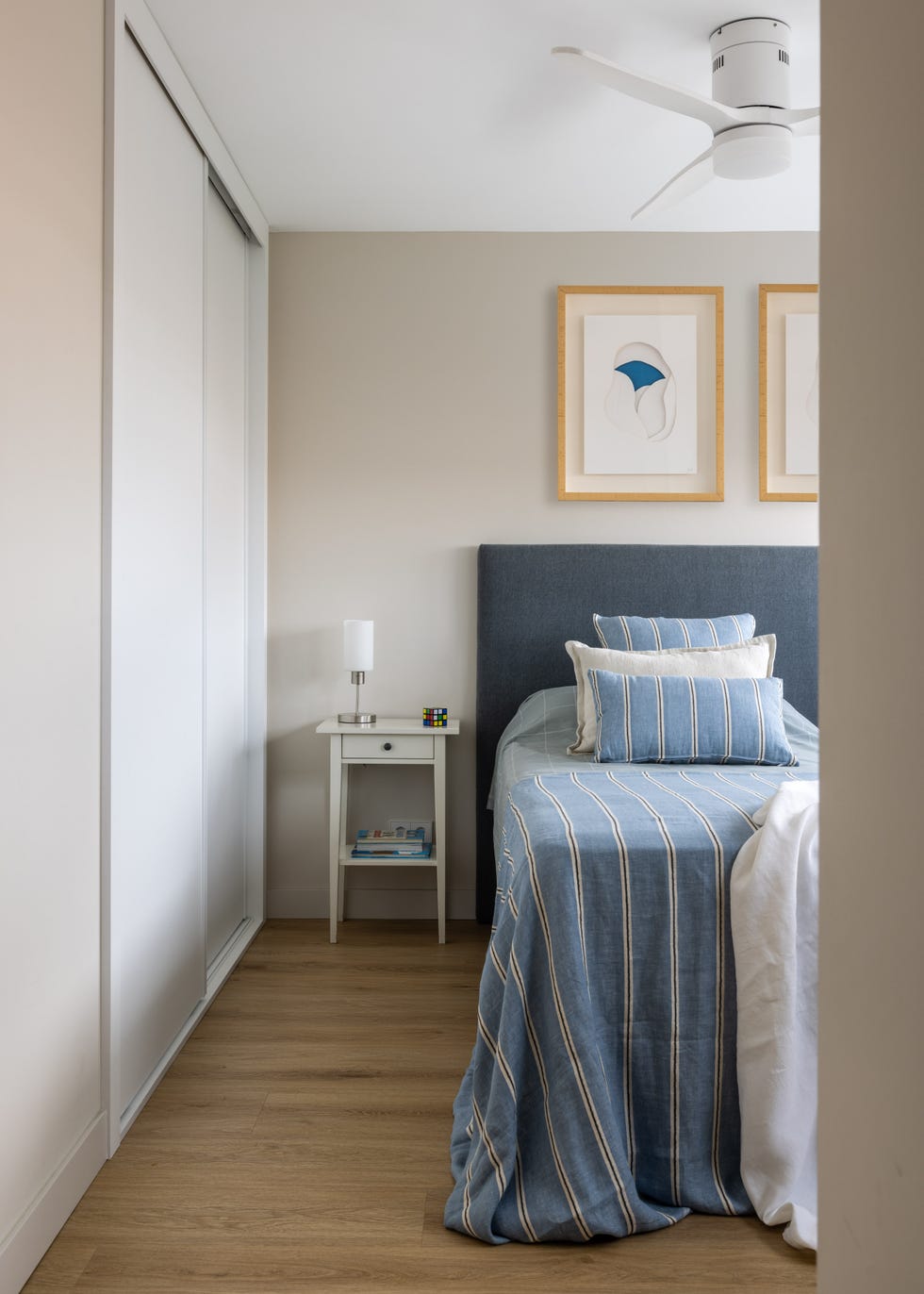 dormitorio con cabecero tapizado en azul y mesita blanca