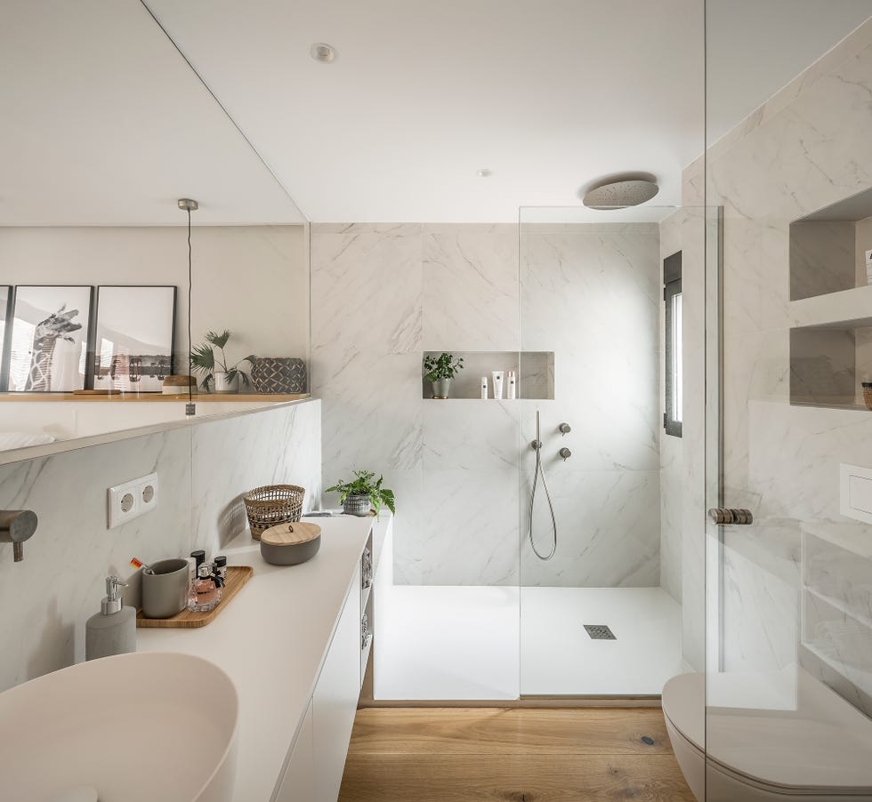 baño con ducha de obra, paredes revestidas en mármol y suelo de madera