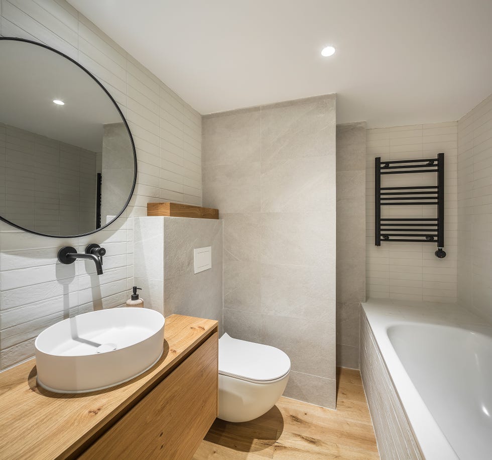 baño con mueble bajo lavamanos, suelo de madera y pared revestida con azulejos blancos