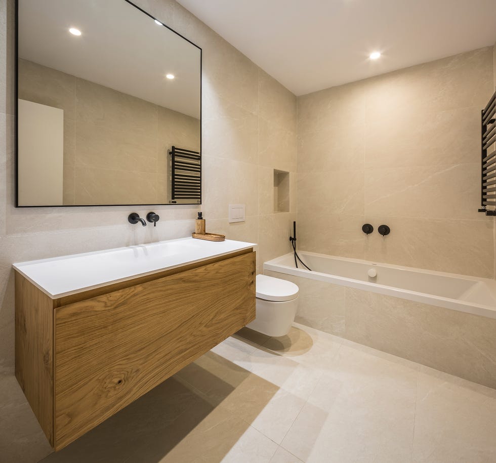 baño con bañera, revestimientos porcelánicos y mueble de madera suspendido