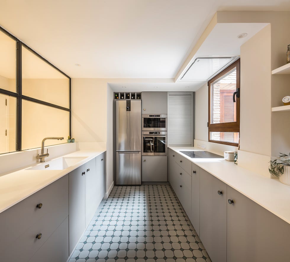 cocina moderna con armarios grises, encimeras blancas y cerramiento de cristal
