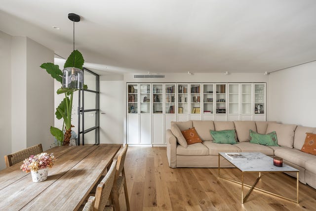 salón abierto con sofá beige, librería empotrada blanca y suelo de madera