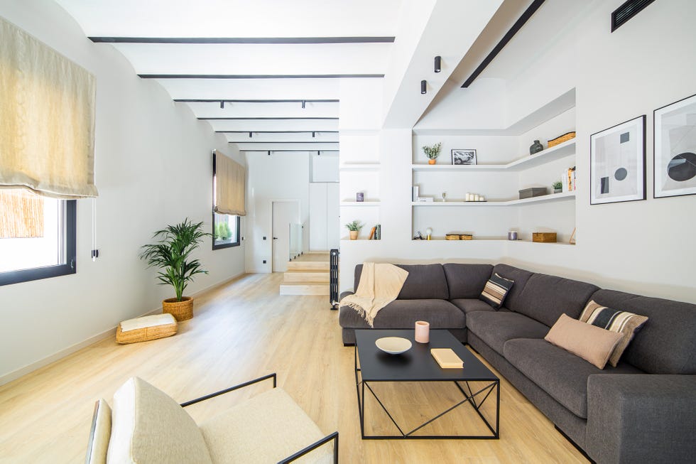 salón abierto moderno con sofá rinconera gris y estantería de obra
