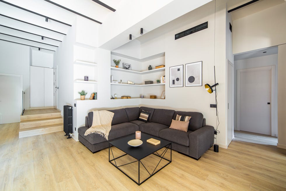 salón abierto moderno con sofá rinconera gris y estantería de obra