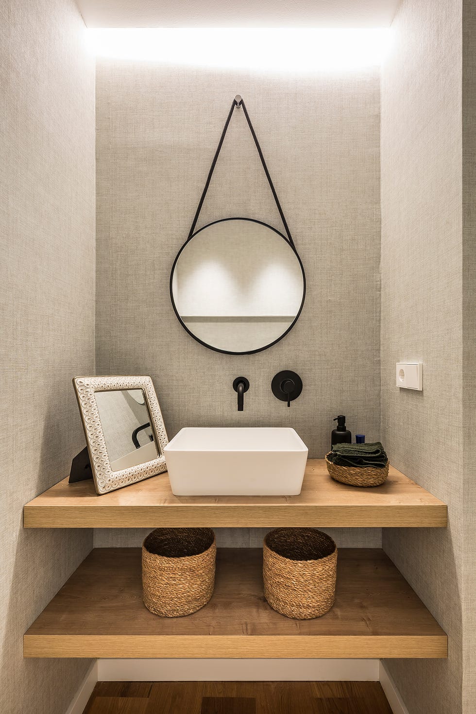 lavabo blanco sobre encimera de madera flotante y espejo de pared redondo con marco de metal negro