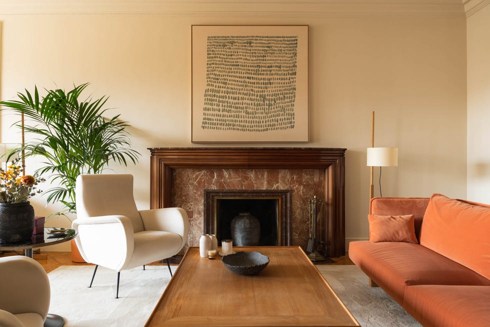 butaca blanca, chimenea, sofá de terciopelo naranja y mesa de centro de madera