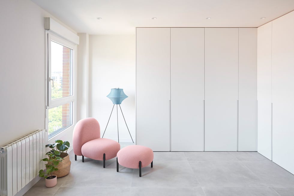 dormitorio con armario en l con puertas blancas y butaca con reposapiés de diseño moderno tapizada en rosa