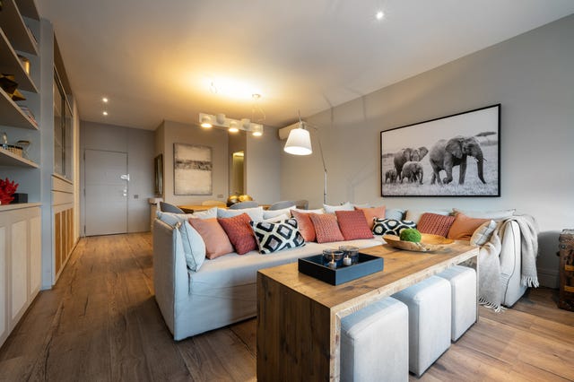 salón open concept decorado con suelo y mesa de centro de madera, sofá gris y cojines en tonos teja