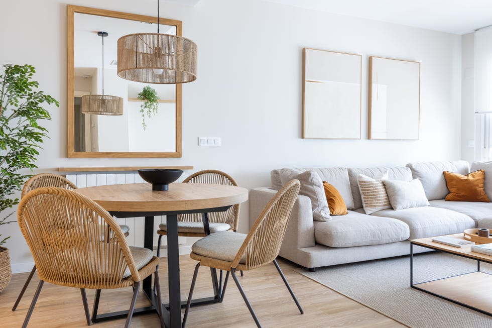 salón comedor con sofá gris y mesa de comedor redonda de madera con sillas de cuerda