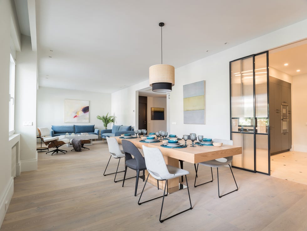 salón comedor abierto a la cocina con mesa de madera alargada, sillas y sofás tapizados en terciopelo