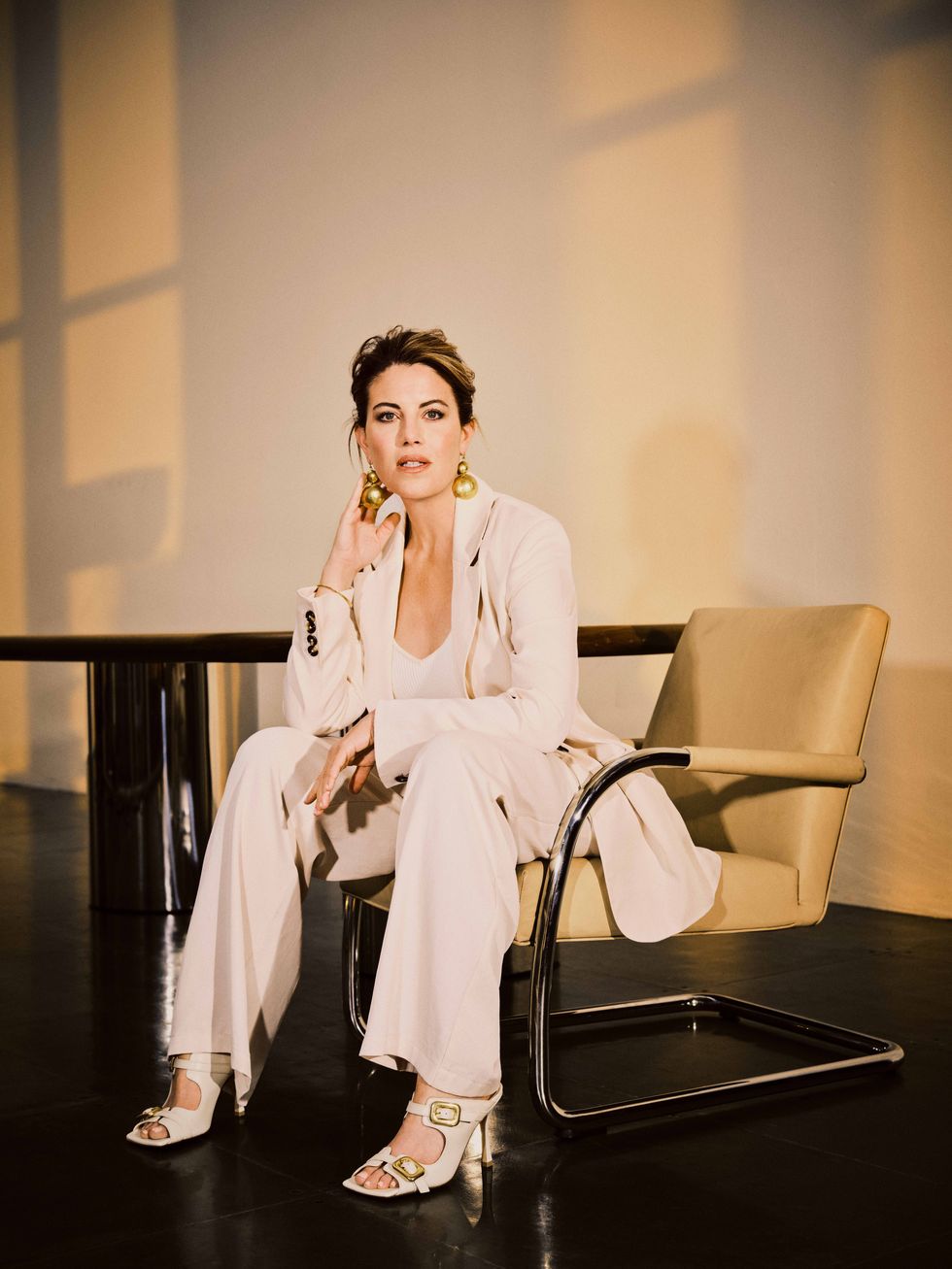 a brunette woman in a cream suit sitting in a chair