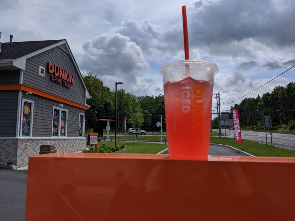 dunkin' pink spritz refresher with green tea base iced drink at a dunkin drivethru with the store in the background