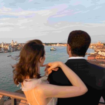 a man and woman kissing on a balcony overlooking a body of water