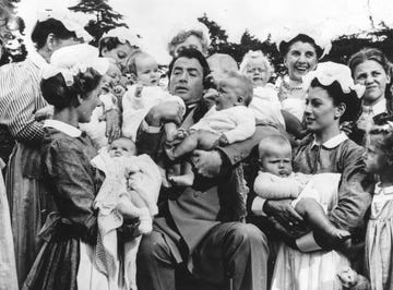 el actor gregory peck sostiene a varios bebés en brazos junto a un grupo de enfermeras en la película 'the million pound note'