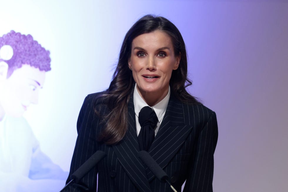 la reina letizia con traje de chaqueta de raya diplomatica y corbata en un acto