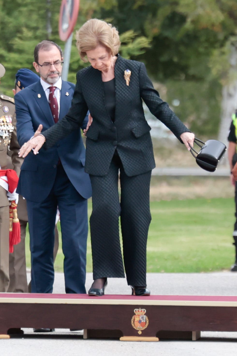 la esposa del rey juan carlos, de negro, ayudada por una persona tras sufrir un desequilibrio